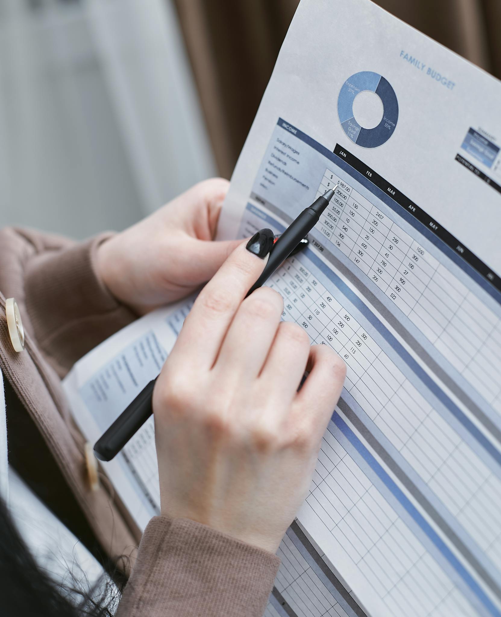 Hands holding a pen review a family budget document with graphs and tables.