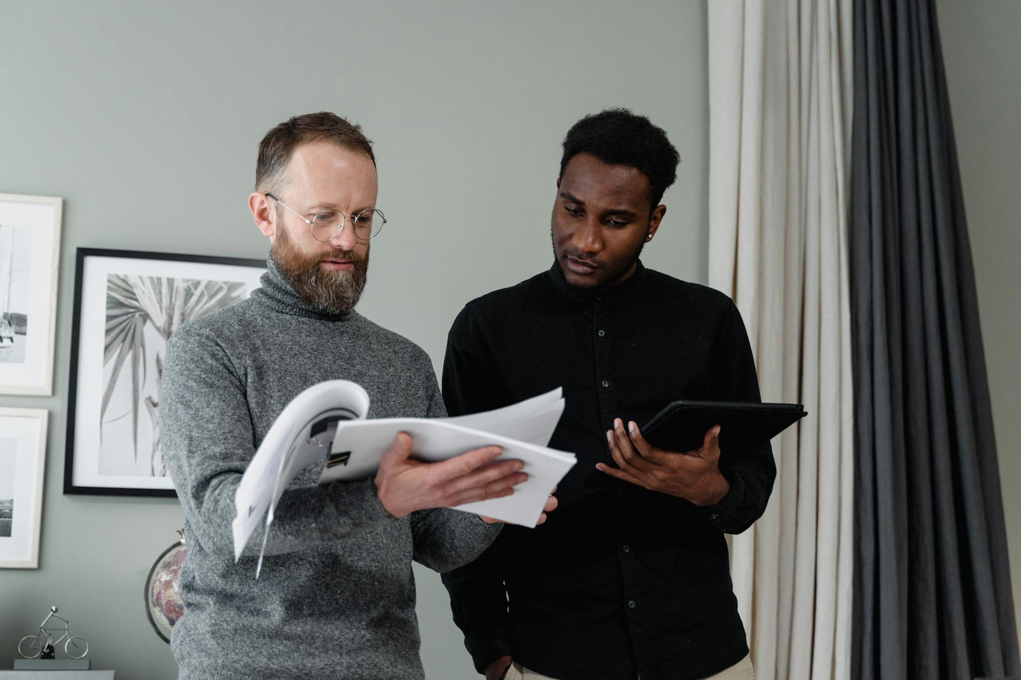 Two businessmen analyzing documents and using a tablet in a modern office setting.